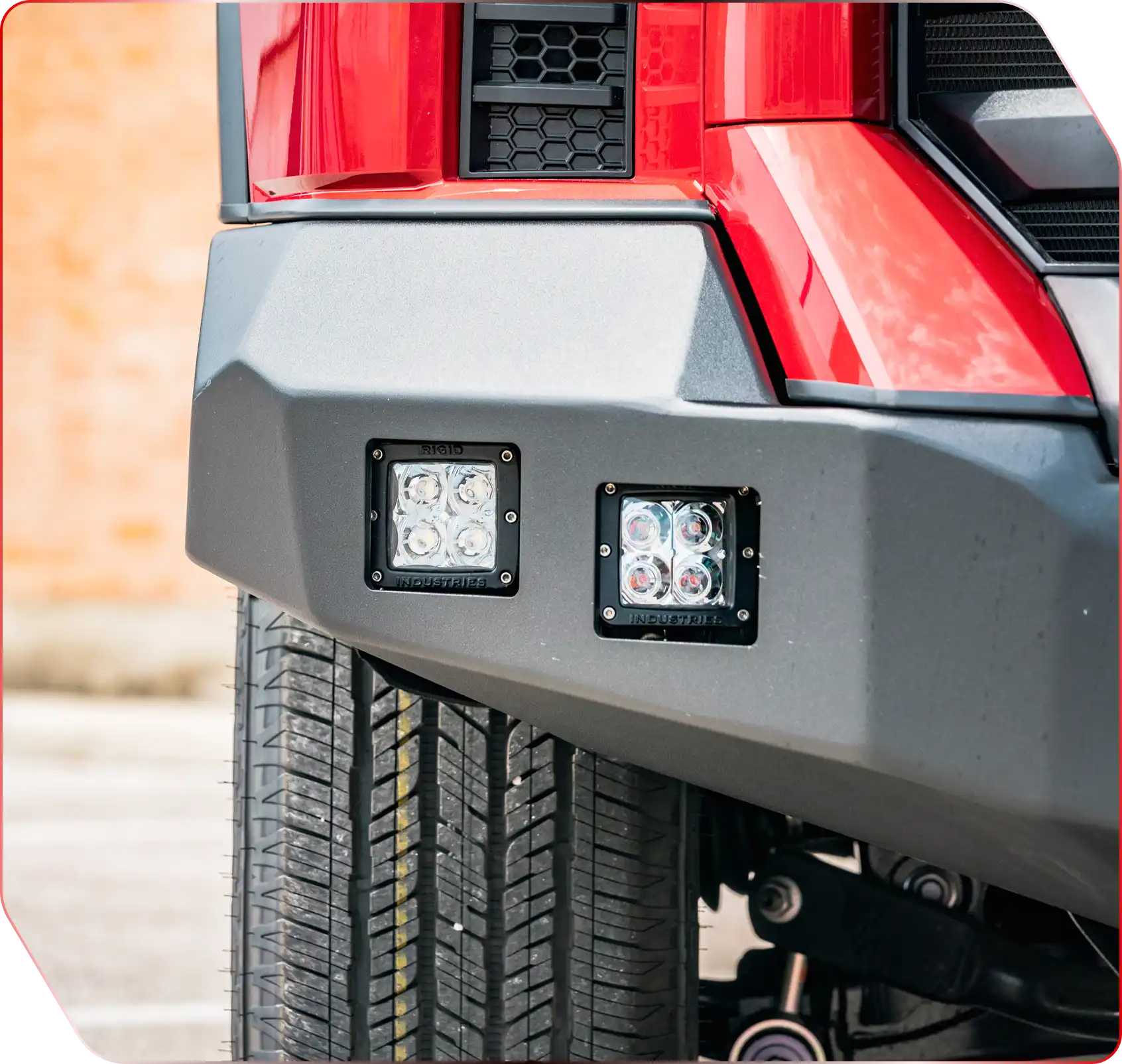 A red truck is parked outdoors, showcasing its front view with visible tires and automotive lighting details.