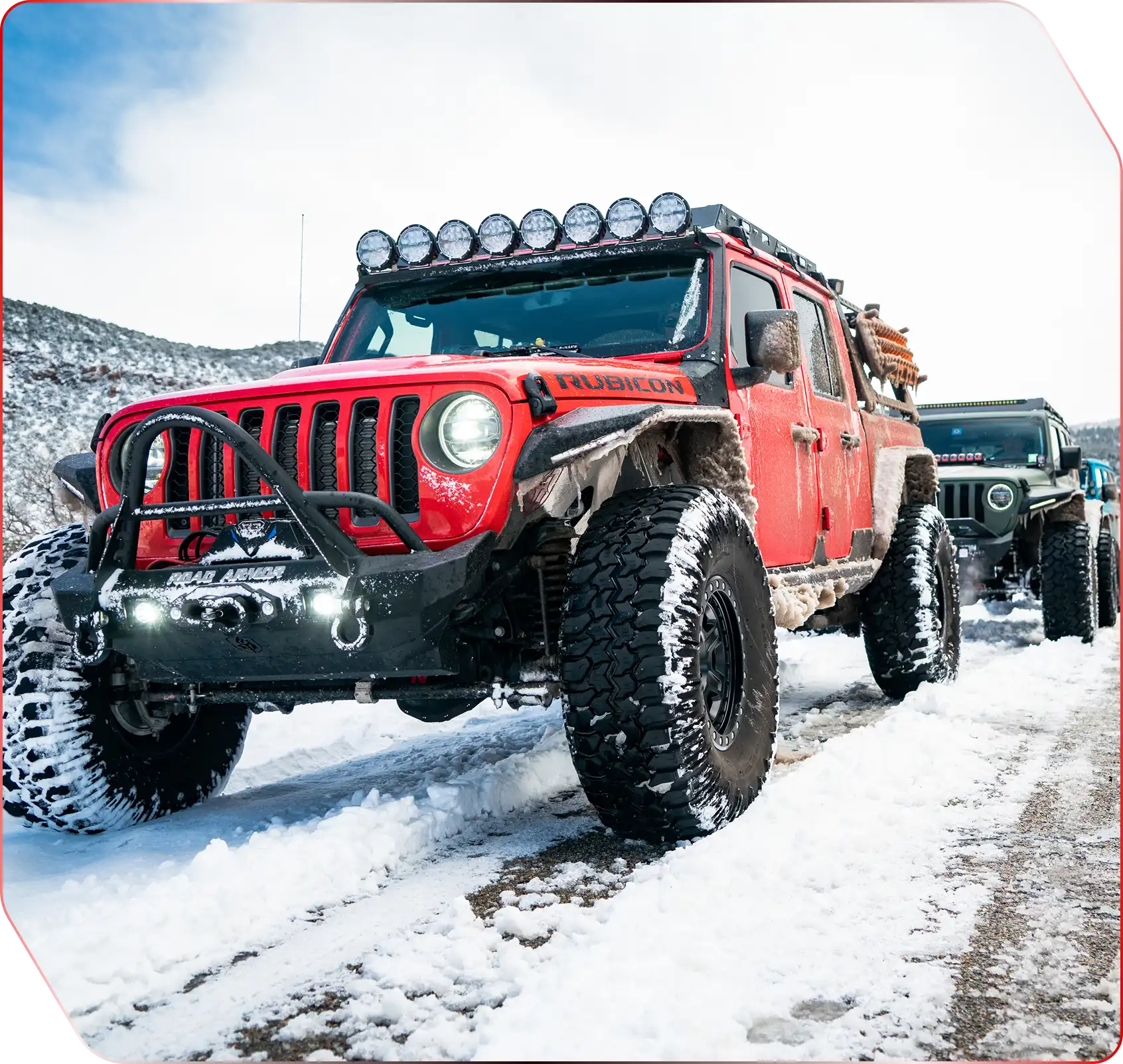 A red truck is parked outdoors, showcasing its front view with visible tires and automotive lighting details.