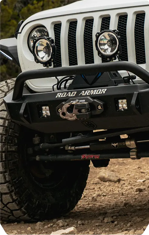 A white jeep parked on a large rock in an outdoor setting, showcasing its rugged tires and off-road capabilities.
