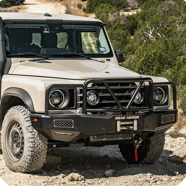A white jeep parked on a large rock in an outdoor setting, showcasing its rugged tires and off-road capabilities.