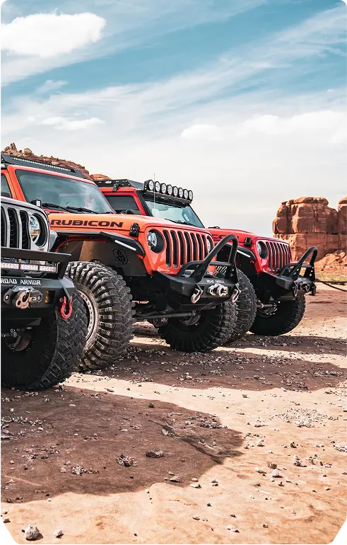 A white jeep parked on a large rock in an outdoor setting, showcasing its rugged tires and off-road capabilities.