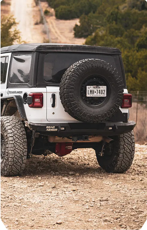 A white jeep parked on a large rock in an outdoor setting, showcasing its rugged tires and off-road capabilities.